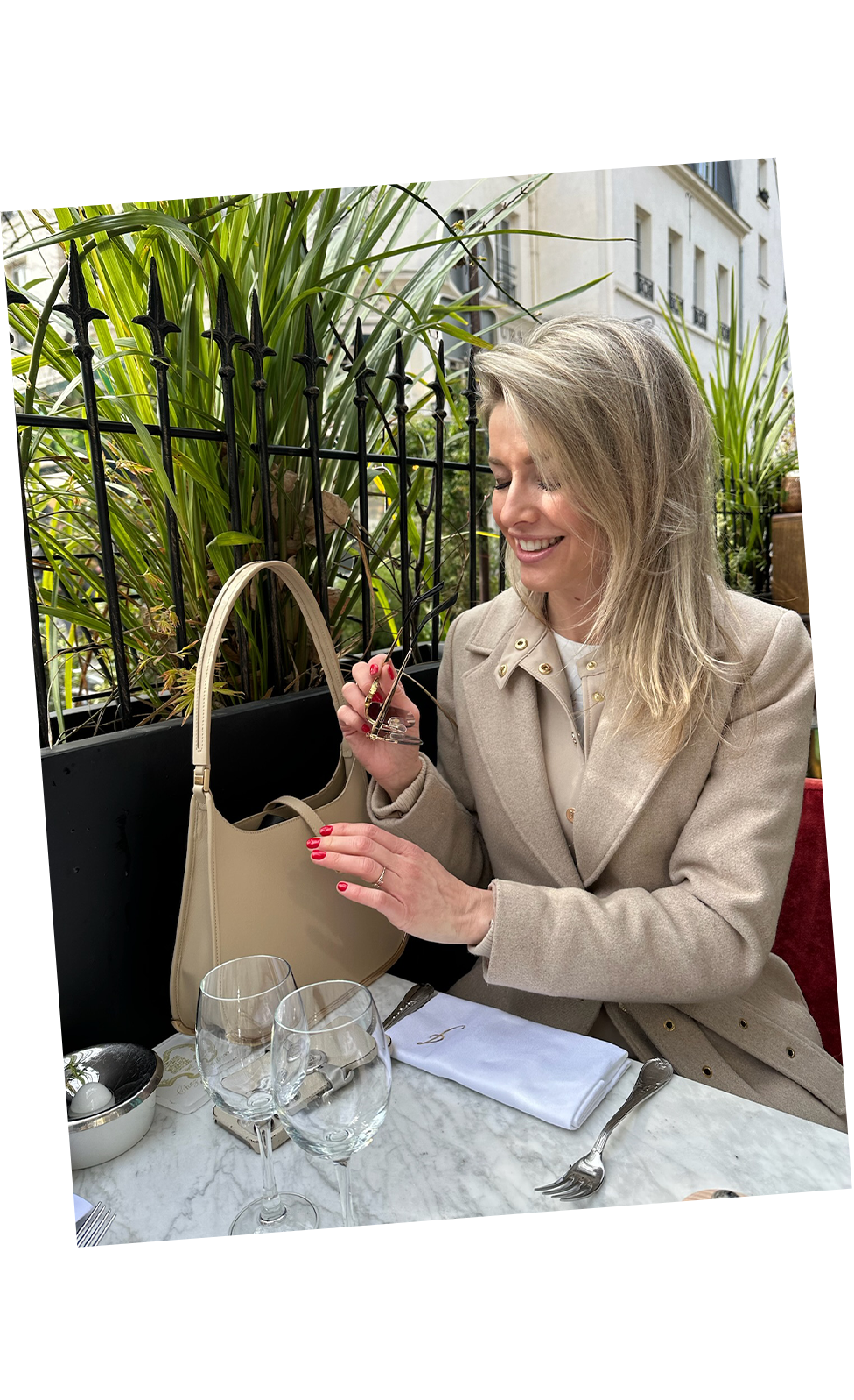 A luxury woman sits on a terrace in Paris, opening a bag placed on a marble table. The leather vaulie bag features a golden metal bottom.