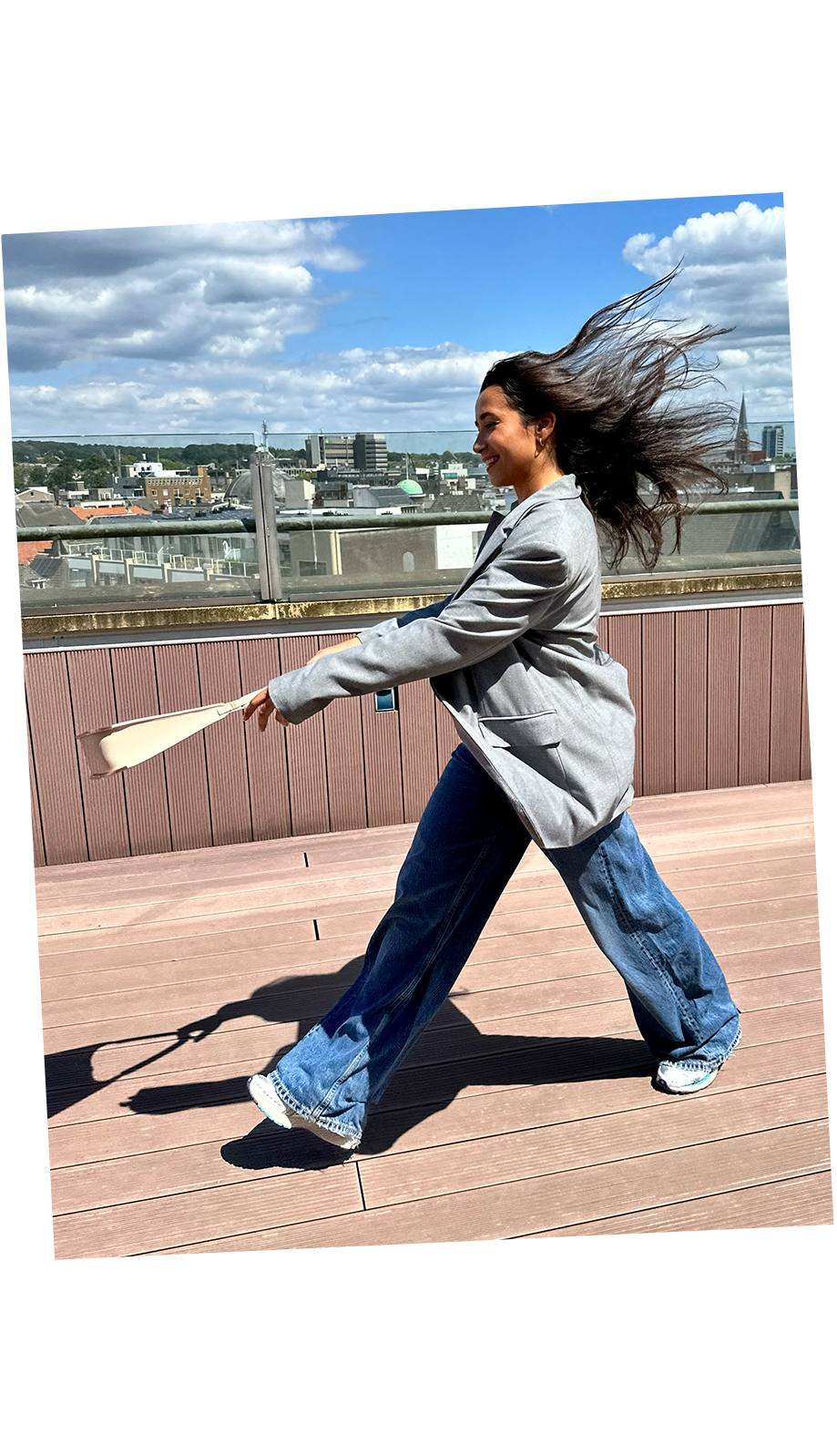 A businesswoman walks by with her hair flowing in the wind, swinging a beige luxury Vaulie bag.