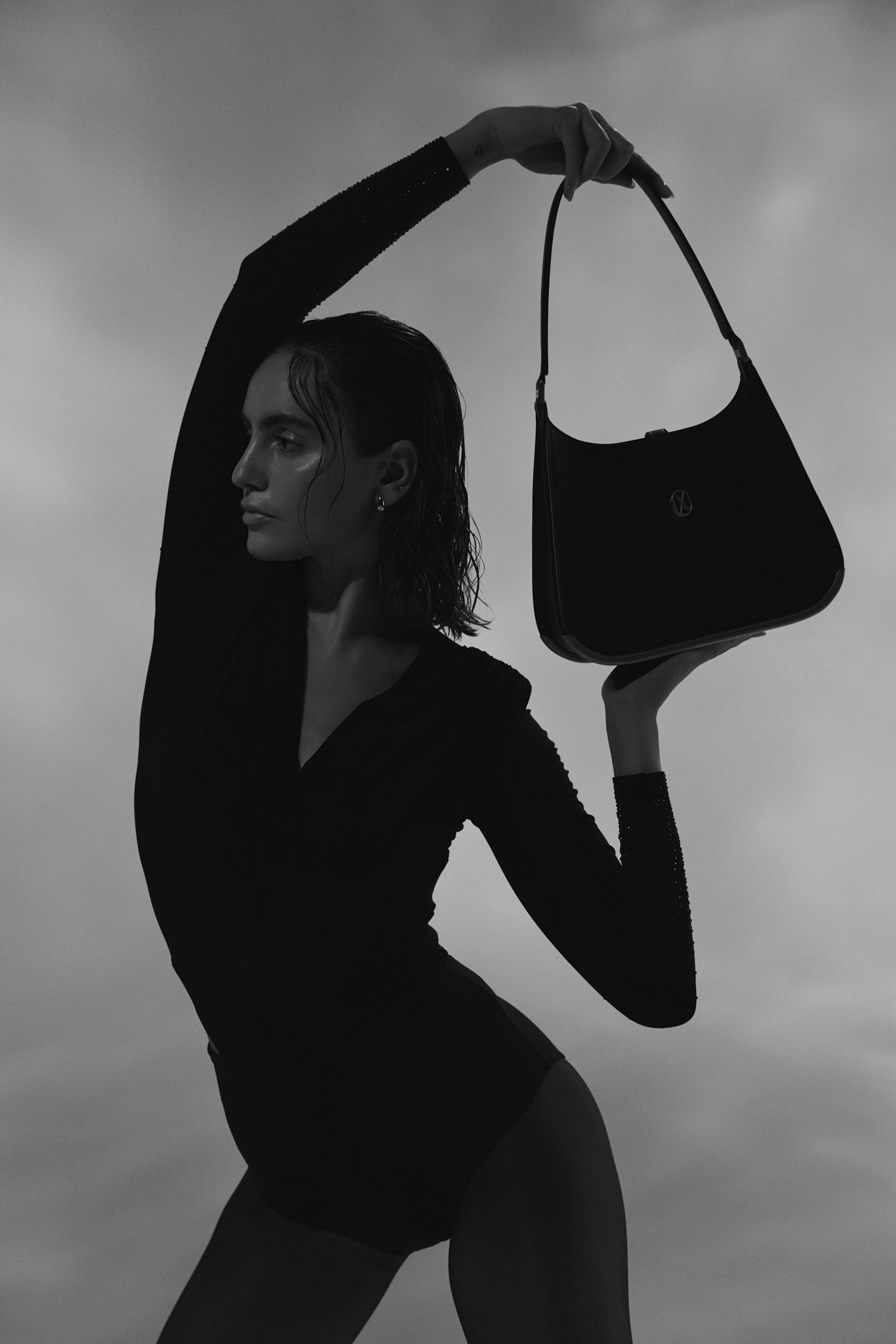 A woman holding a luxury bag over her head with one hand and supporting it with the other. The curved design of the bag complements the curves of her body.