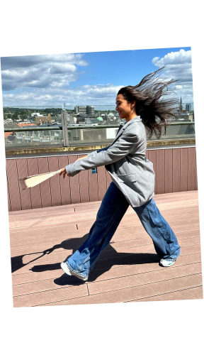 A businesswoman walks by with her hair flowing in the wind, swinging a beige luxury Vaulie bag.